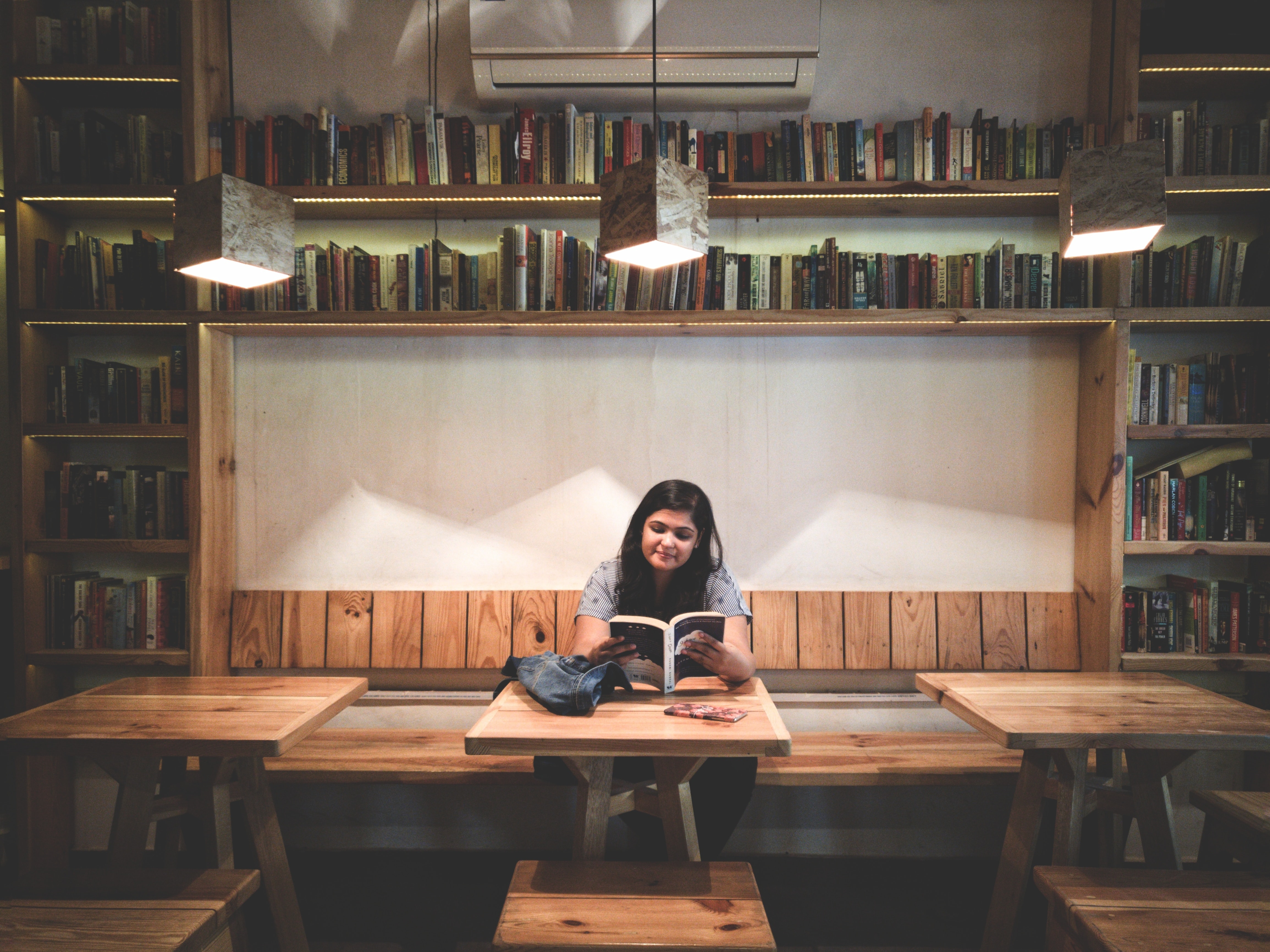 Decorative, person reading a book at a table, surrounded by books